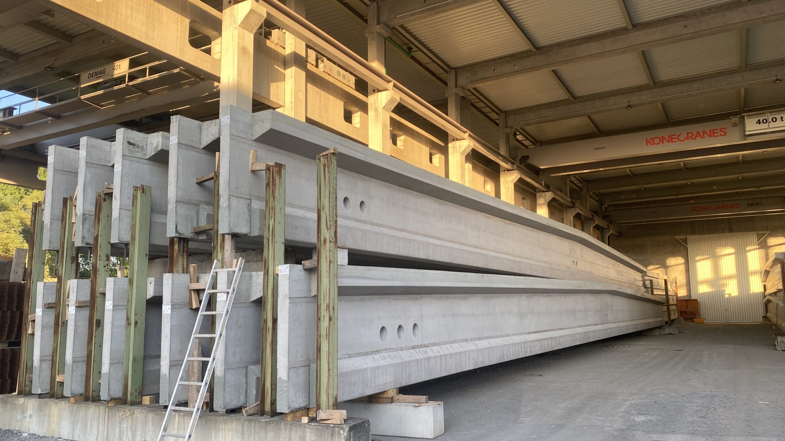 Gestapelte Betonfertigteile in einer Produktionshalle mit Kranbahn.
